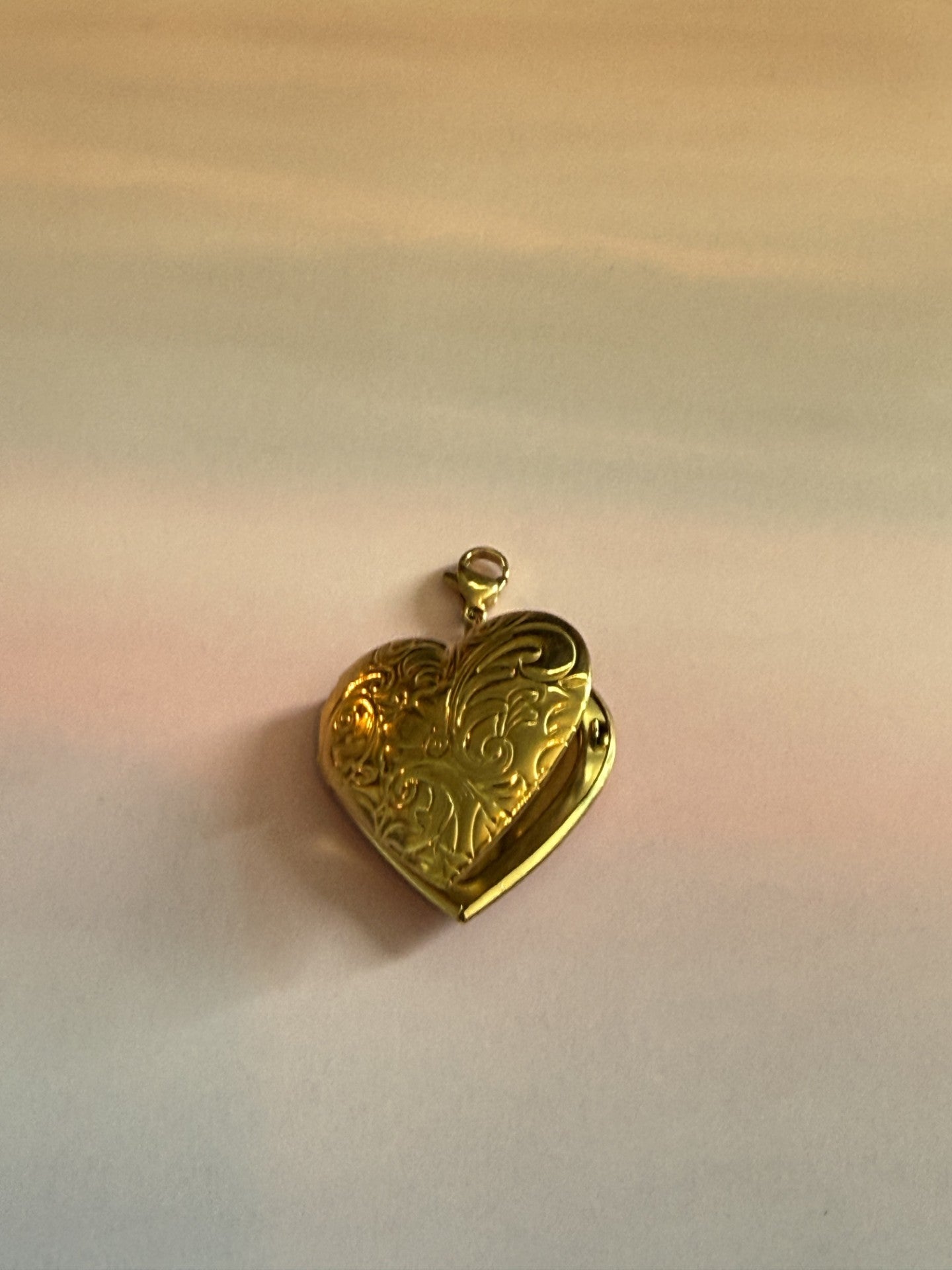 Gouden RVS hart medaillon bedel met fotovak voor ketting op gekleurde achtergrond.