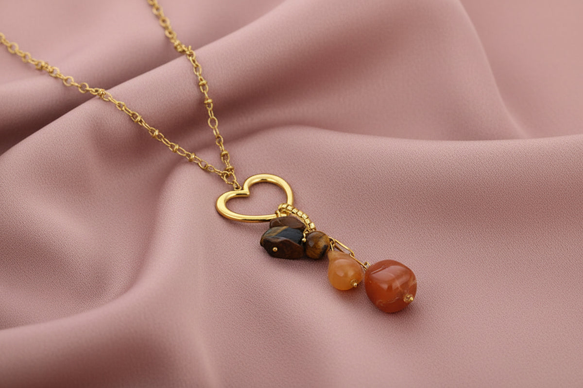 Glow Mystic in Style gouden stainless steel ketting met open hart en bruine kralenbedel gepresenteerd op roze gedrapeerd kleed.