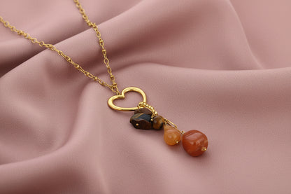 Glow Mystic in Style gouden stainless steel ketting met open hart en bruine kralenbedel gepresenteerd op roze gedrapeerd kleed.