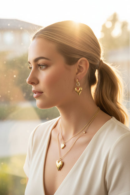 "Close-up van de details van de gouden hart oorbellen met koraalroze steentjes en zoetwaterparels gedragen door een model.