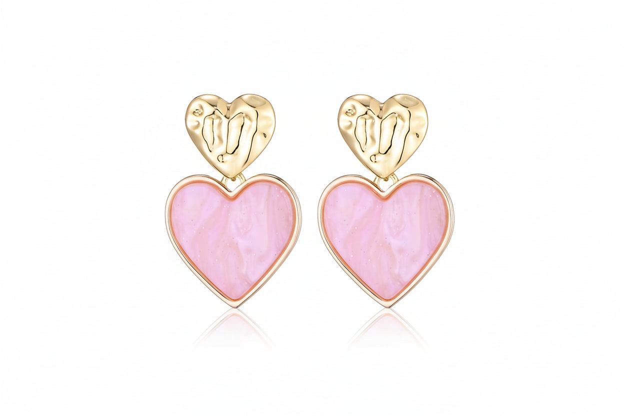 Goudkleurige hart oorbellen met roze hart hanger close -up- romantische statement oorbellen