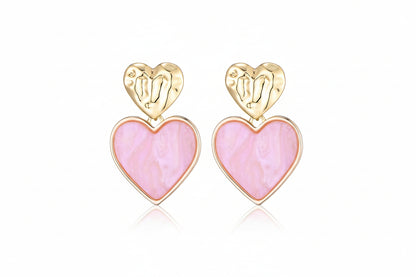 Goudkleurige hart oorbellen met roze hart hanger close -up- romantische statement oorbellen