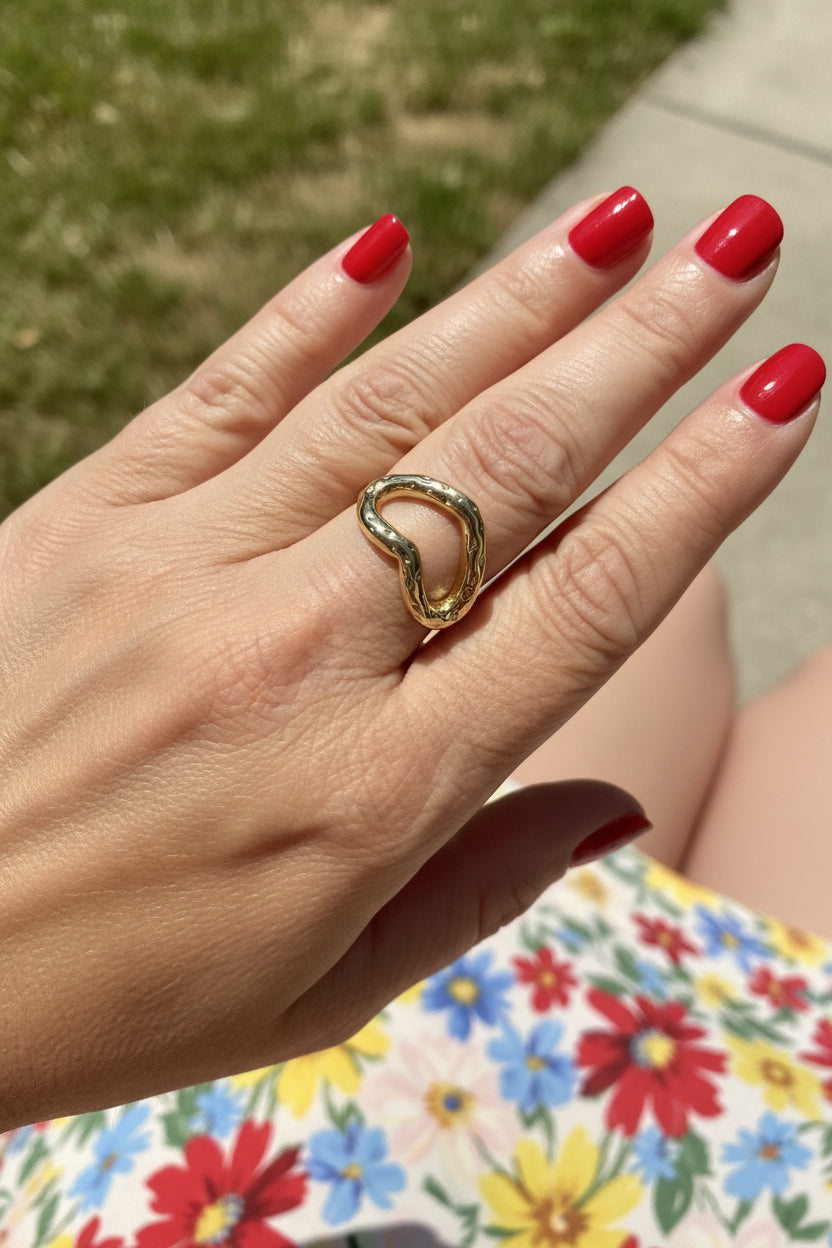 Luxe gouden golvende hart ring gedragen om de vinger van een vrouw met rode nagellak op een zonnige dag.