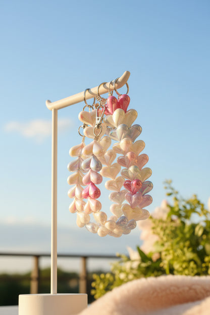 "twee handgemaakte telefoonkoorden met parelmoer hartjes in wit en pastelkleuren hangend aan een witte display tegen een blauwe lucht."