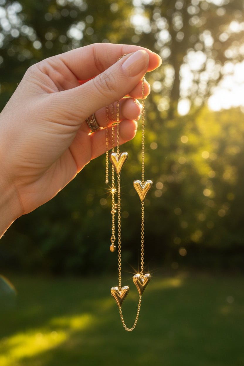 Luxe goudkleurige lange harstjes ketting van waterproof RVS sfeervol vastgehouden in een hand in de natuur, glanzend in de warme zonnestralen.