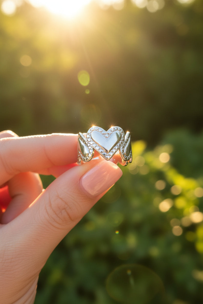 Zilveren Amour ring met hartenpatroon vastgehouden in de hand met een dromerige, zonnige achtergrond