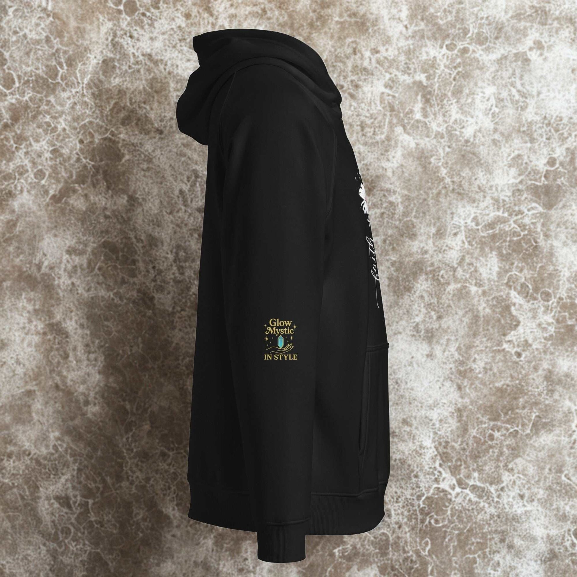 Side view of black unisex eco raglan hoodie with floral print and Glow Mystic branding on sleeve against textured background