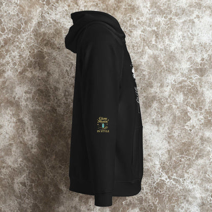 Side view of black unisex eco raglan hoodie with floral print and Glow Mystic branding on sleeve against textured background