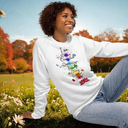 woman wearing white unisex organic raglan sweatshirt with colorful text design sitting outdoors in a field