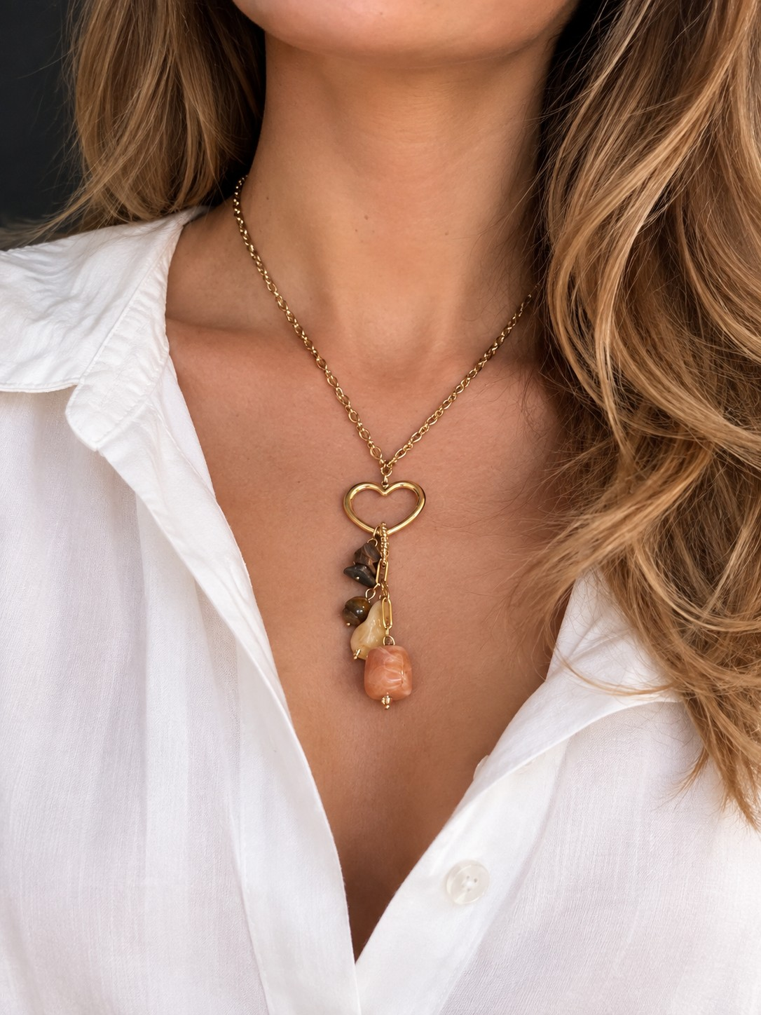 Model draagt de Glow Mystic in Style gouden ketting met open hart en bruine kralen bij een witte blouse