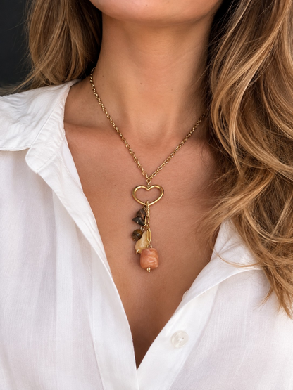 Model draagt de Glow Mystic in Style gouden ketting met open hart en bruine kralen bij een witte blouse