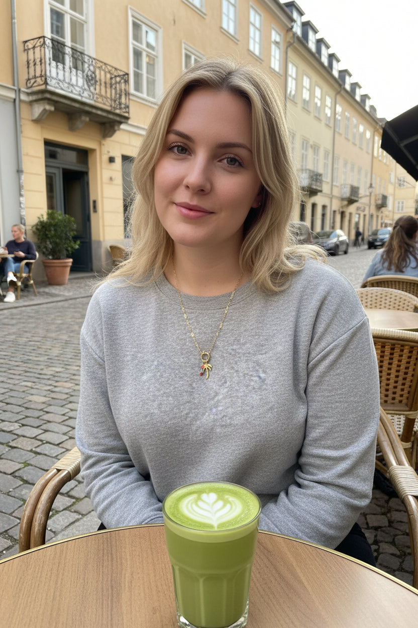 Jonge vrouw op een terras die de palmboomketting draagt op tafel staat een glas matcha