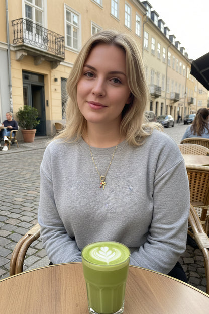 Jonge vrouw op een terras die de palmboomketting draagt op tafel staat een glas matcha
