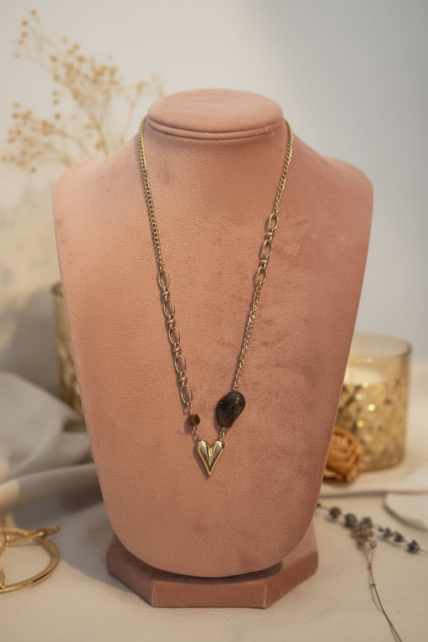 Close-up van de bruine organische kraal, facetkraal en het gouden 3D hartje aan de ketting op een oud roze buste