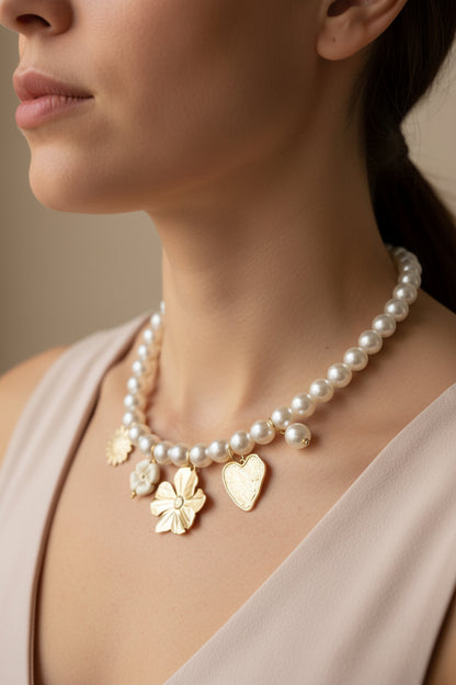 Een vrolijke close-up van een vrouw die de Stainless Steel Parelketting met goudkleurige charms draagt. De korte ketting (42-45 cm) valt elegant in de hals en toont de goudkleurige bedels en parels die subtiel 'zwieren' bij beweging, tegen een zacht verlichte achtergrond.