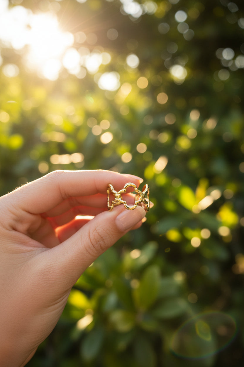 "Artistieke foto van de gouden Lucky Clover ring vastgehouden in het zonlicht met een natuurlijke groene achtergrond."