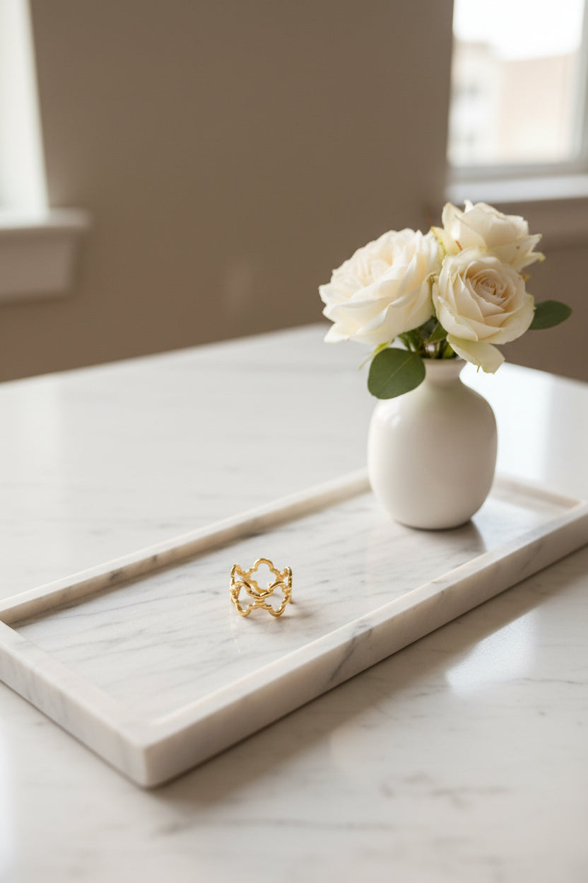 "Artistieke foto van de gouden Lucky Clover ring gepresenteerd op een langwerpige marmeren schaal met een wit vaasje met witte rozen erbij gepresenteerd.