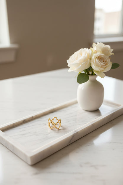 "Artistieke foto van de gouden Lucky Clover ring gepresenteerd op een langwerpige marmeren schaal met een wit vaasje met witte rozen erbij gepresenteerd.