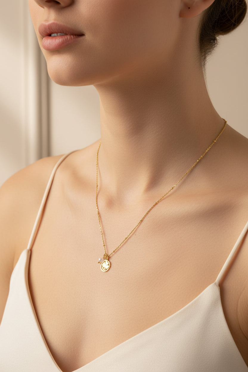 Goudkleurige ketting met een klavertje vier met hartje bedel en een regenboog maansteen kraal, gedragen door een vrouw. Een subtiele focus op het sieraad als een betekenisvolle vruchtbaarheids-talisman of symbool voor vrouwelijke energie.