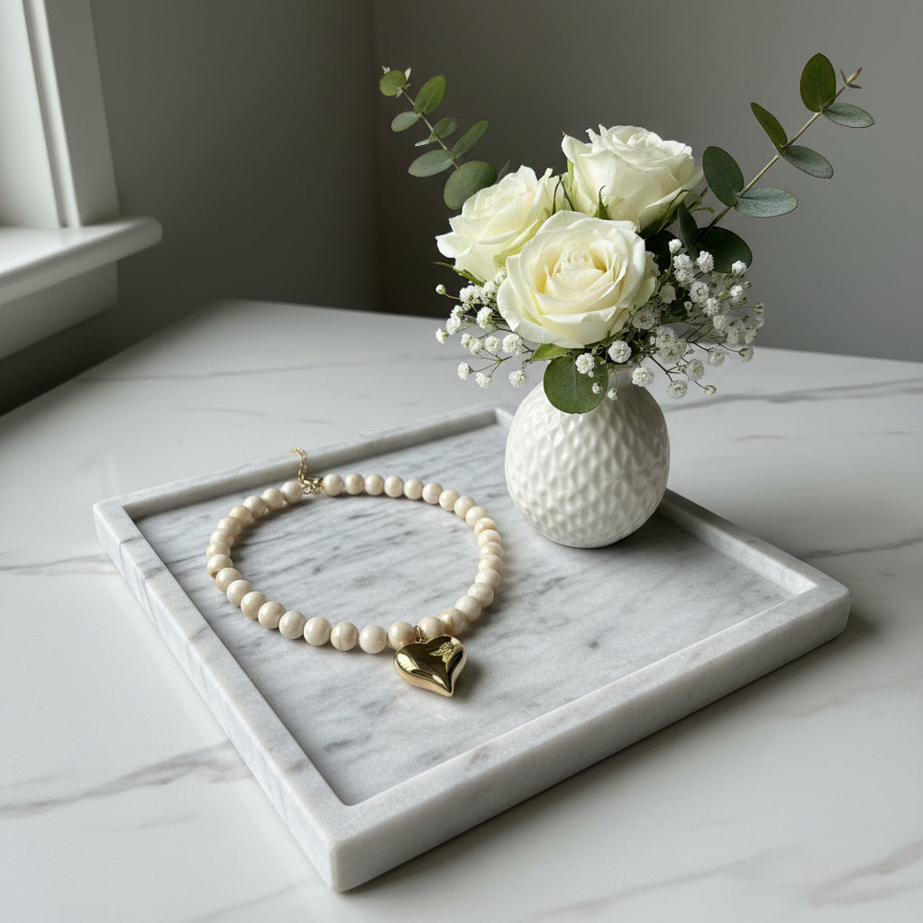 Close-up van de gepolijste goudkleurige harthanger en de beige-witte gevlamde kralen van de Stainless Steel ketting."