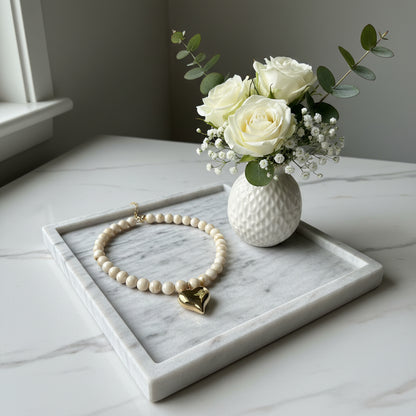 Close-up van de gepolijste goudkleurige harthanger en de beige-witte gevlamde kralen van de Stainless Steel ketting."