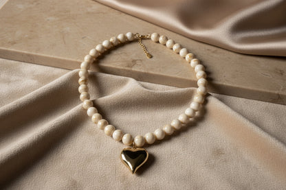 Close-up van de gepolijste goudkleurige harthanger en de beige-witte gevlamde kralen van de Stainless Steel ketting.
