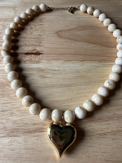 Close-up van de gepolijste goudkleurige harthanger en de beige-witte gevlamde kralen van de Stainless Steel ketting."