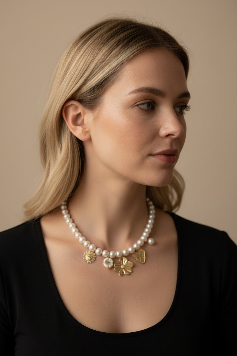 Een vrolijke close-up van een vrouw die de Stainless Steel Parelketting met goudkleurige charms draagt. De korte ketting (42-45 cm) valt elegant in de hals en toont de goudkleurige bedels en parels die subtiel 'zwieren' bij beweging, tegen een zacht verlichte achtergrond.