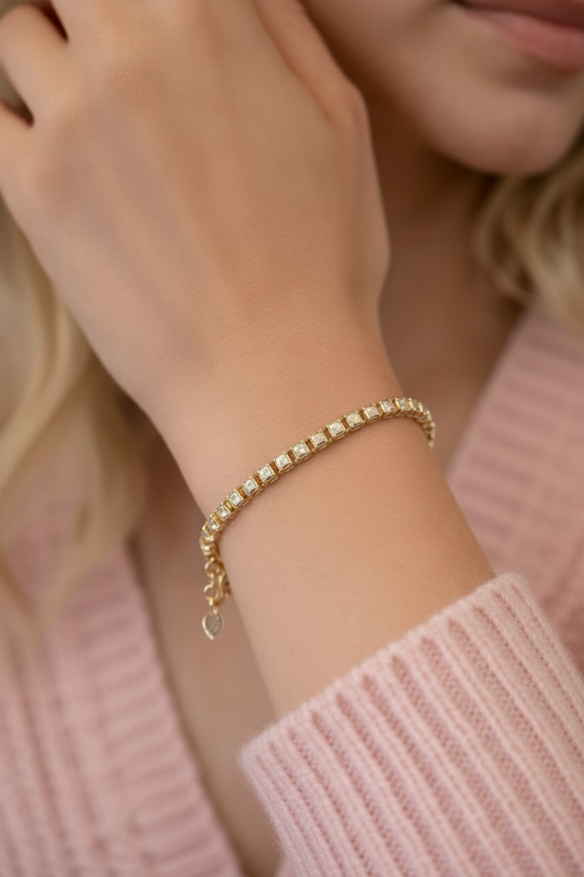 Detailopname van een luxe gouden kristalarmband gedragen om een pols, gecombineerd met een roze gebreide trui voor een elegante uitstraling.