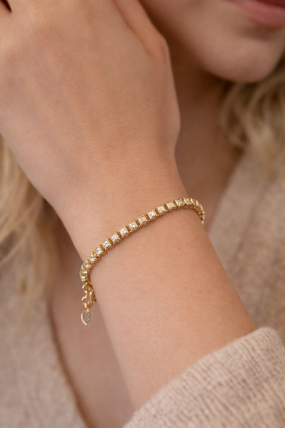 Detailopname van een luxe gouden kristalarmband gedragen om een pols, gecombineerd met een beige gebreide trui voor een elegante uitstraling.