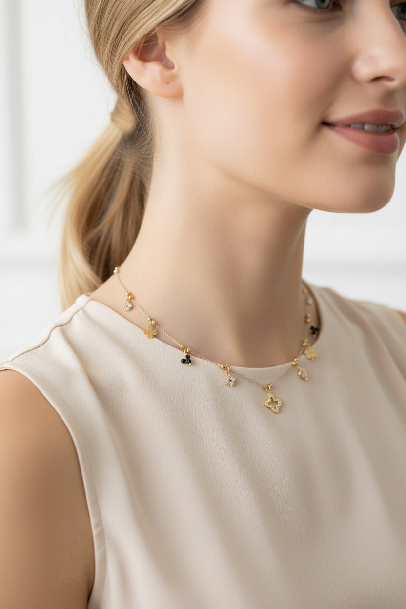 Korte goudkleurige RVS kristalketting met fijne klaver-bedeltjes, elegant gedragen hoog in de hals door een model met een witte blouse.
