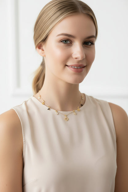 Korte goudkleurige RVS kristalketting met fijne klaver-bedeltjes, elegant gedragen hoog in de hals door een model met een witte blouse.