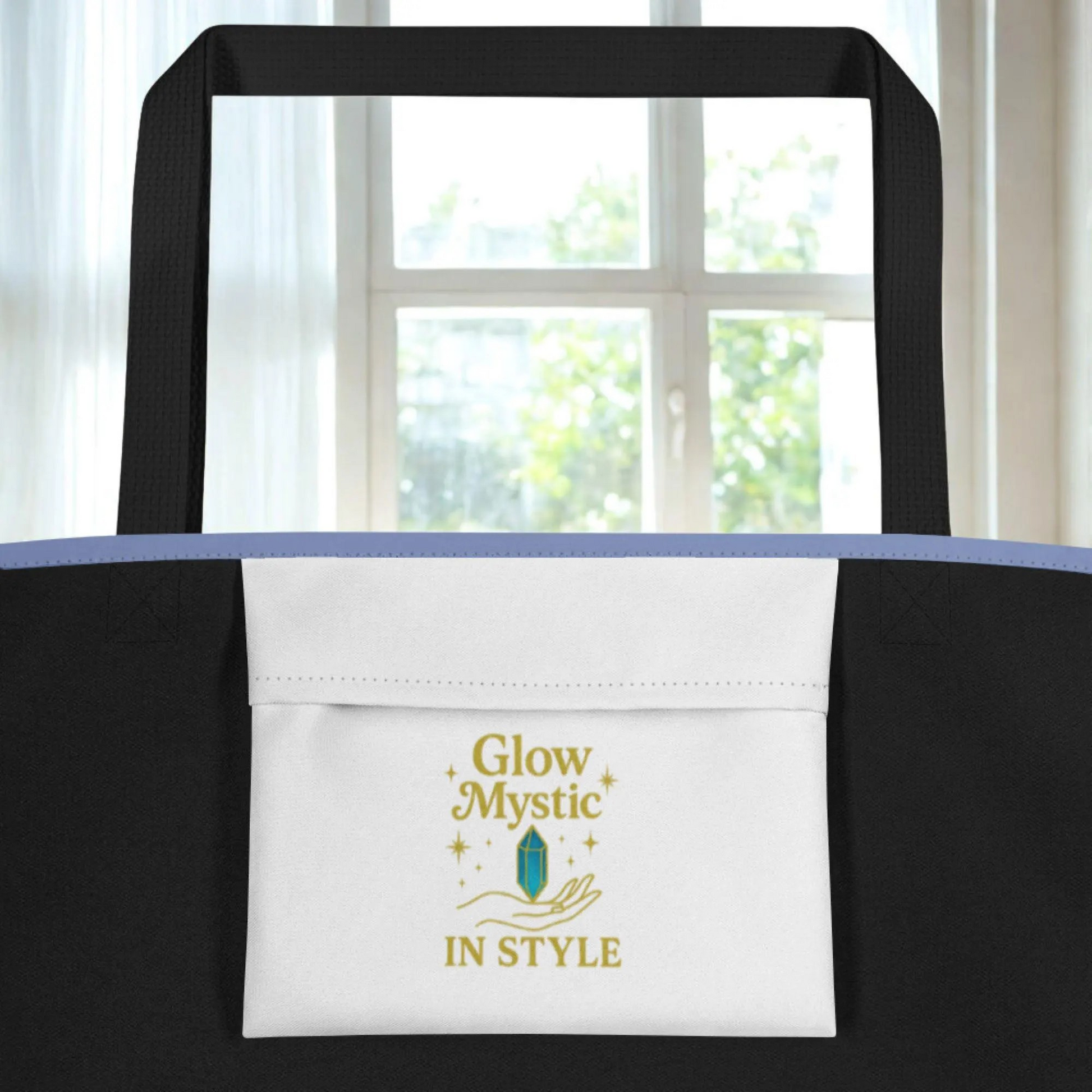 close-up of a black Floral Mystic Tote Bag with white front pocket and gold Glow Mystic logo near window background