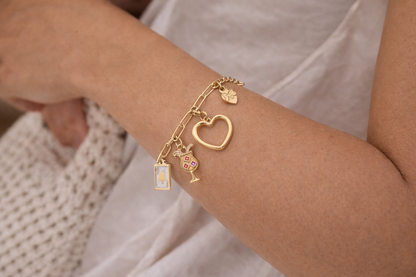 “Close-up van een gouden bedelarmband met hart, klaver aas en cocktail glas bedels gedragen om de pols.