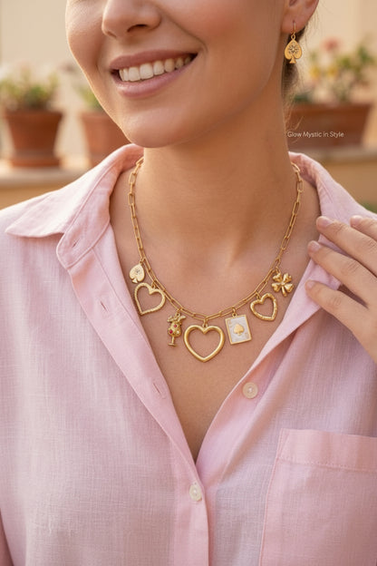 Een model met een zacht roze linnen blouse draagt de goudkleurige RVS Vegas & Cocktail bedelketting met bijpassende oorbellen in een warme, zonnige setting.