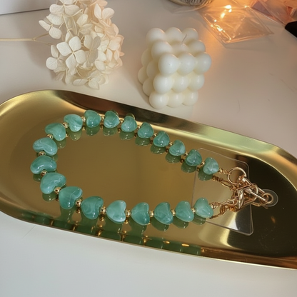 Gow Mystic in Style groen hartjes telefoonkoord op een goudkleurige schaal met kaarsje en bloemetje eromheen.