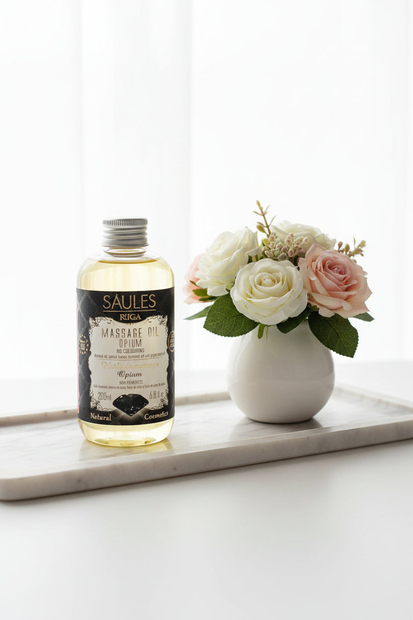 aules Fabrika luxe massageolie Opium 200ml doseerfles met zwarte diamant op het label - Glow Mystic in Style gepresenteerd op een langwerpige marmeren schaal met een vaasje met witte en roze rozen ernaast.
