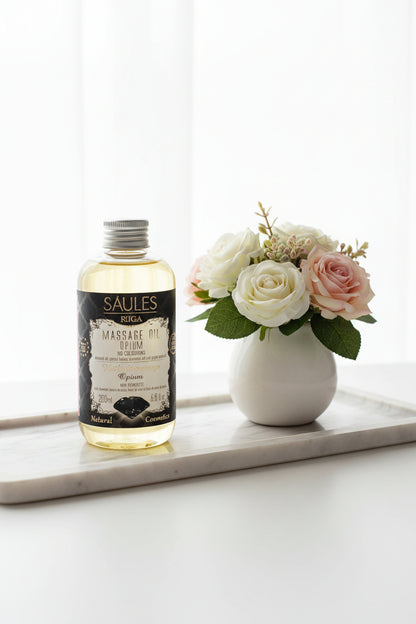 aules Fabrika luxe massageolie Opium 200ml doseerfles met zwarte diamant op het label - Glow Mystic in Style gepresenteerd op een langwerpige marmeren schaal met een vaasje met witte en roze rozen ernaast.