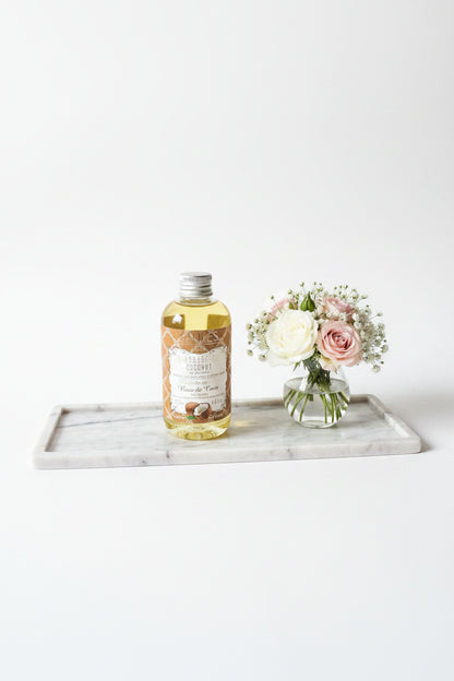 Saules Fabrika massageolie Coconut 200ml op een luxe marmeren plateau naast een vaasje met zachtroze en witte rozen - Glow Mystic in Style.