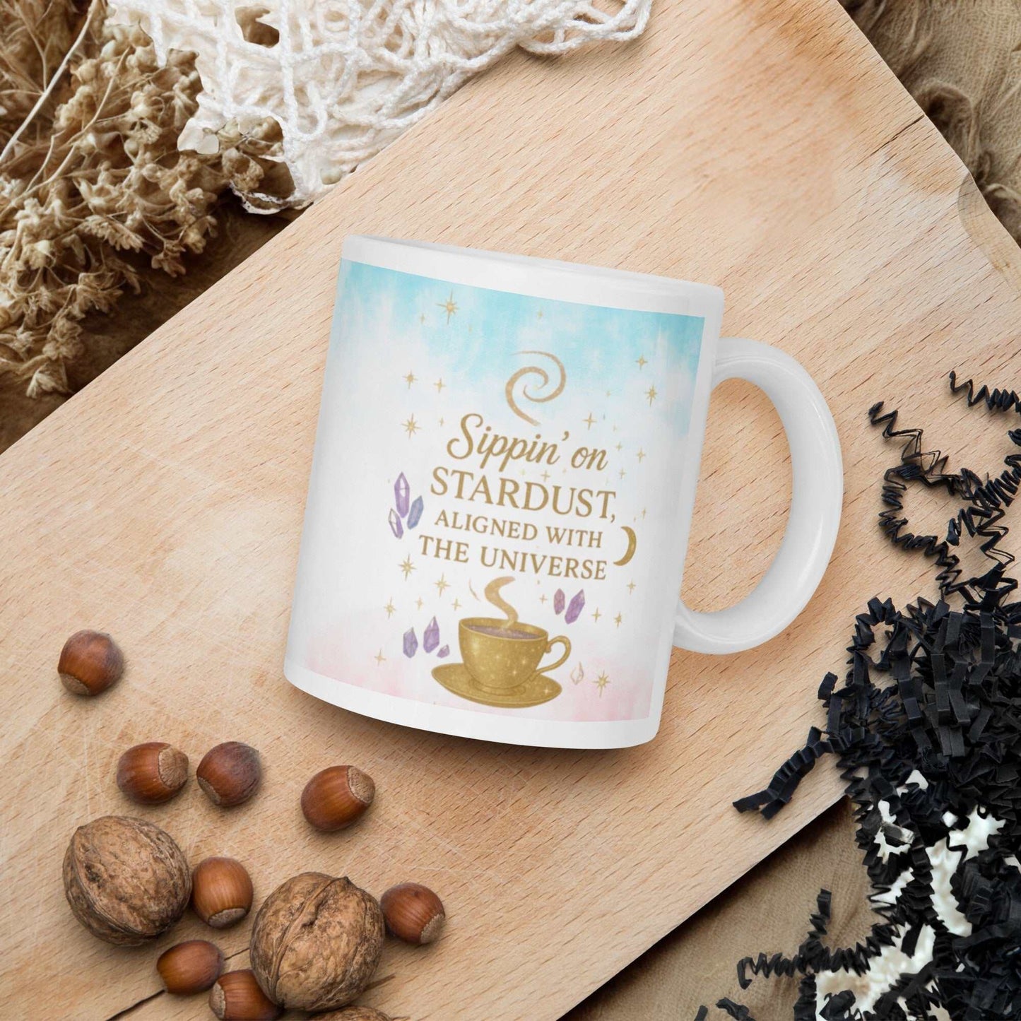 white ceramic Sippin on Stardust Coffee Mug with celestial design and golden text on wooden tray with nuts and decorative elements