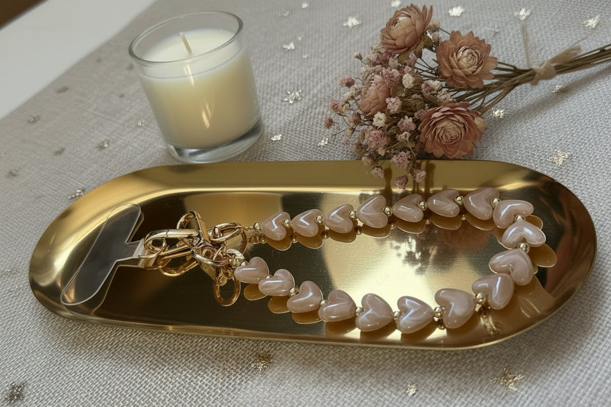 Zijaanzicht van een mocha kleur hartjes telefoonkoord van Glow Mystic in Style op een goudkleurige glanzende schaal met 2 lifestyle producten eromheen