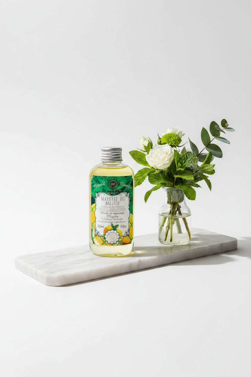 Saules Fabrika massageolie Mojito 200ml op een marmeren plateau naast een vaasje met frisse groene bladeren - Glow Mystic in Style.