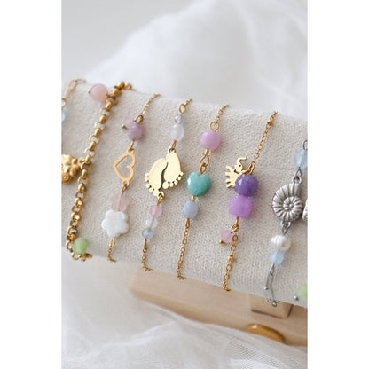 "Het goudkleurige Geluksarmbandje met Olifantje gepresenteerd op een luxe beige sieradendisplay, omringd door andere fijne edelsteenarmbanden uit de spirituele collectie van Glow Mystic in Style."
