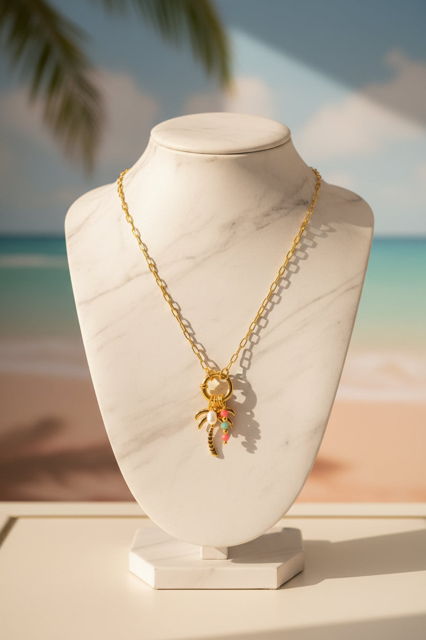 Goudkleurige schakelketting met een palmboom bedeltje en gekleurde kralen op een witte display buste.