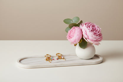 Palmboom oorbellen als mock up op een marmeren langwerpige schaal met een wit vaasje en roze bloemen en een takje eucalyptus erin.