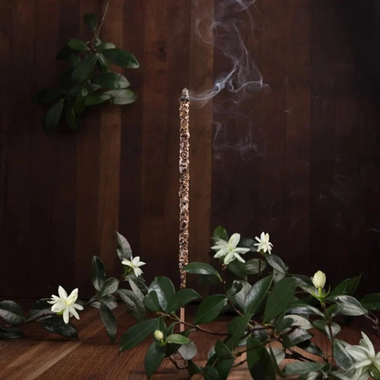 Sfeerfoto van een brandend Sagrada Madre Palo Santo wierookstokje omringd door champa takjes.