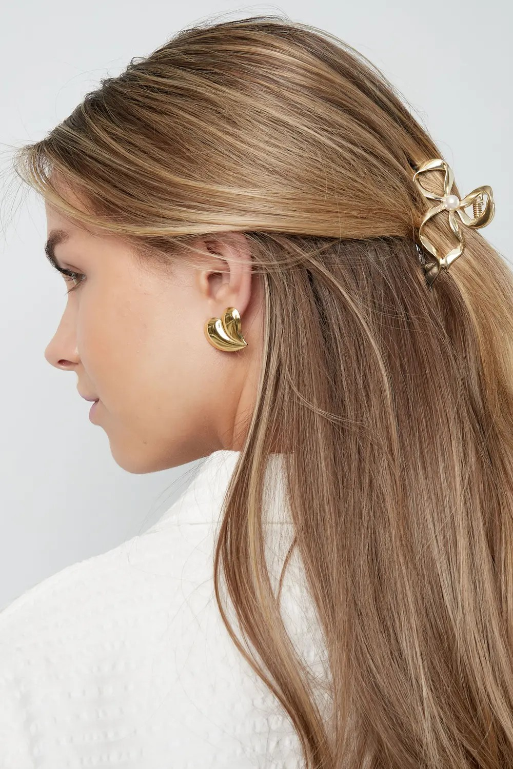 Model van de zijkant met blond haar in een elegante half-up look, vastgezet met de gouden strik haarklem met parel.
