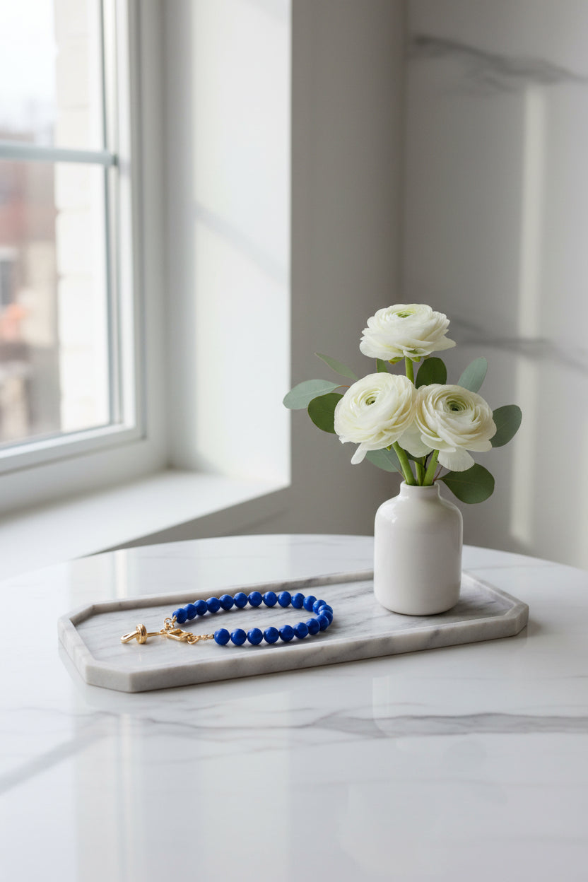 Royal Bleu telefoonkoord met ronde kralen en goudkleurige sluiting, elegant gepresenteerd p een marmeren dienblad naast witte bloemen in een vaasje.