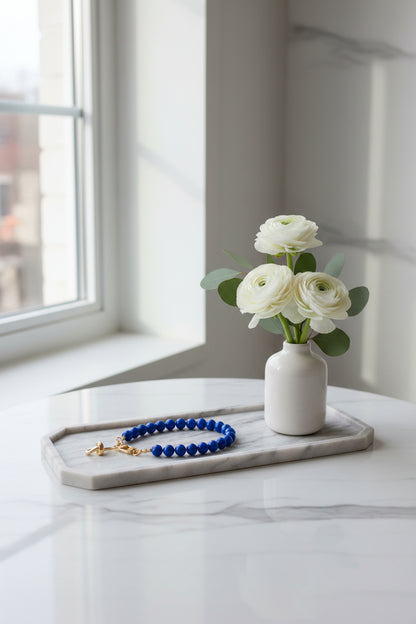 Royal Bleu telefoonkoord met ronde kralen en goudkleurige sluiting, elegant gepresenteerd p een marmeren dienblad naast witte bloemen in een vaasje.