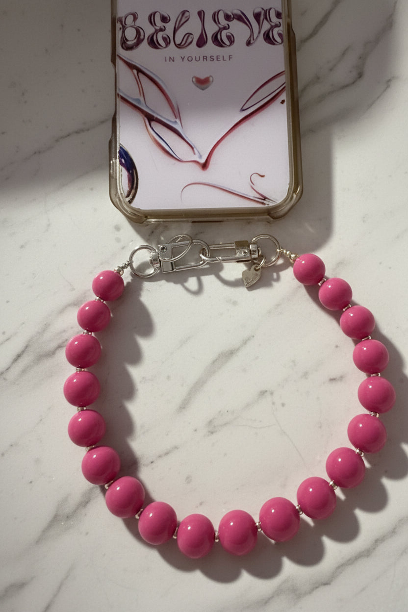 Handgemaakte fuchsia roze phone charm van Glow Mystic in Style, bevestigd aan een telefoonhoesje en gepresenteerd op een luxe witte marmeren achtergrond.